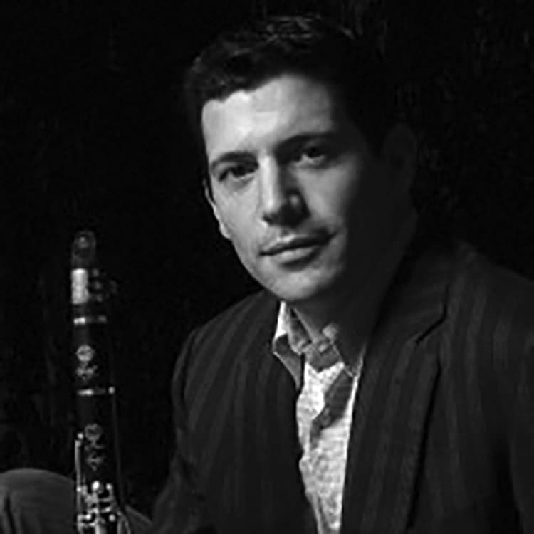 A man in a suit sitting next to a saxophone