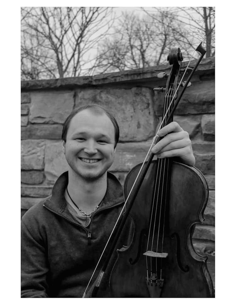A man holding a violin in front of a stone wall