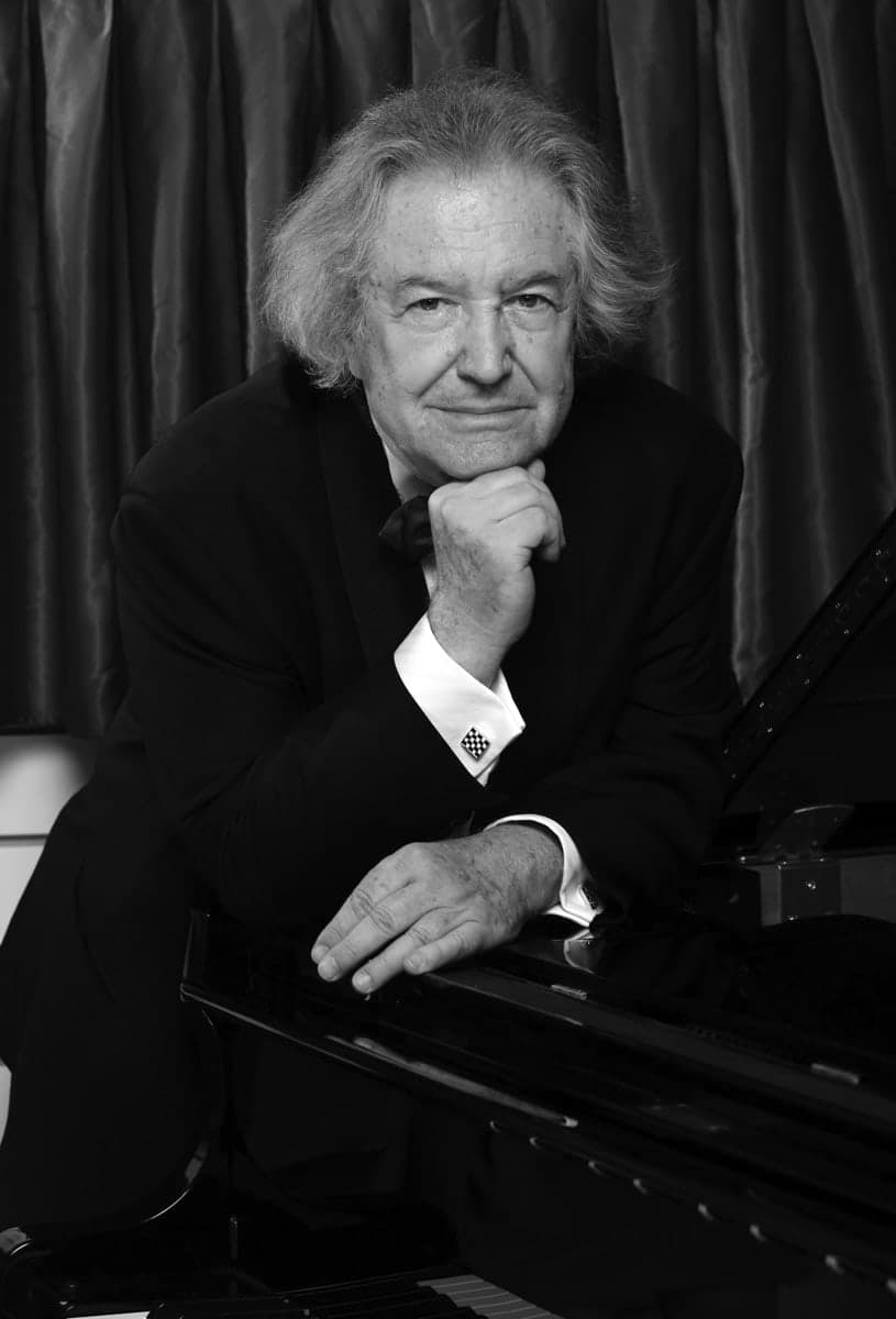 A black and white photo of a man leaning on a piano
