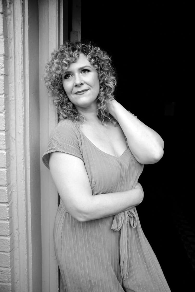 A black and white photo of a woman leaning against a wall