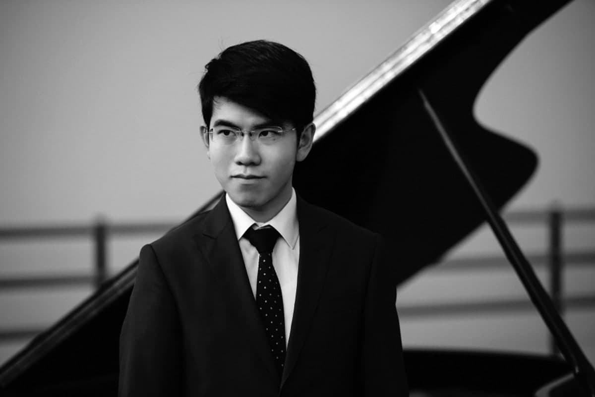 A man in a suit and tie standing next to a piano