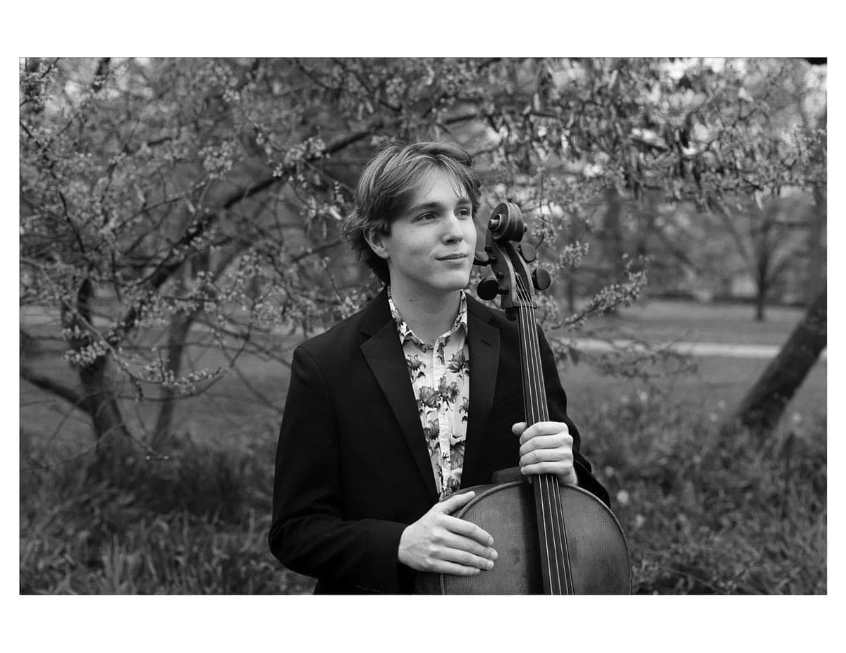 A man holding a cello in front of a tree