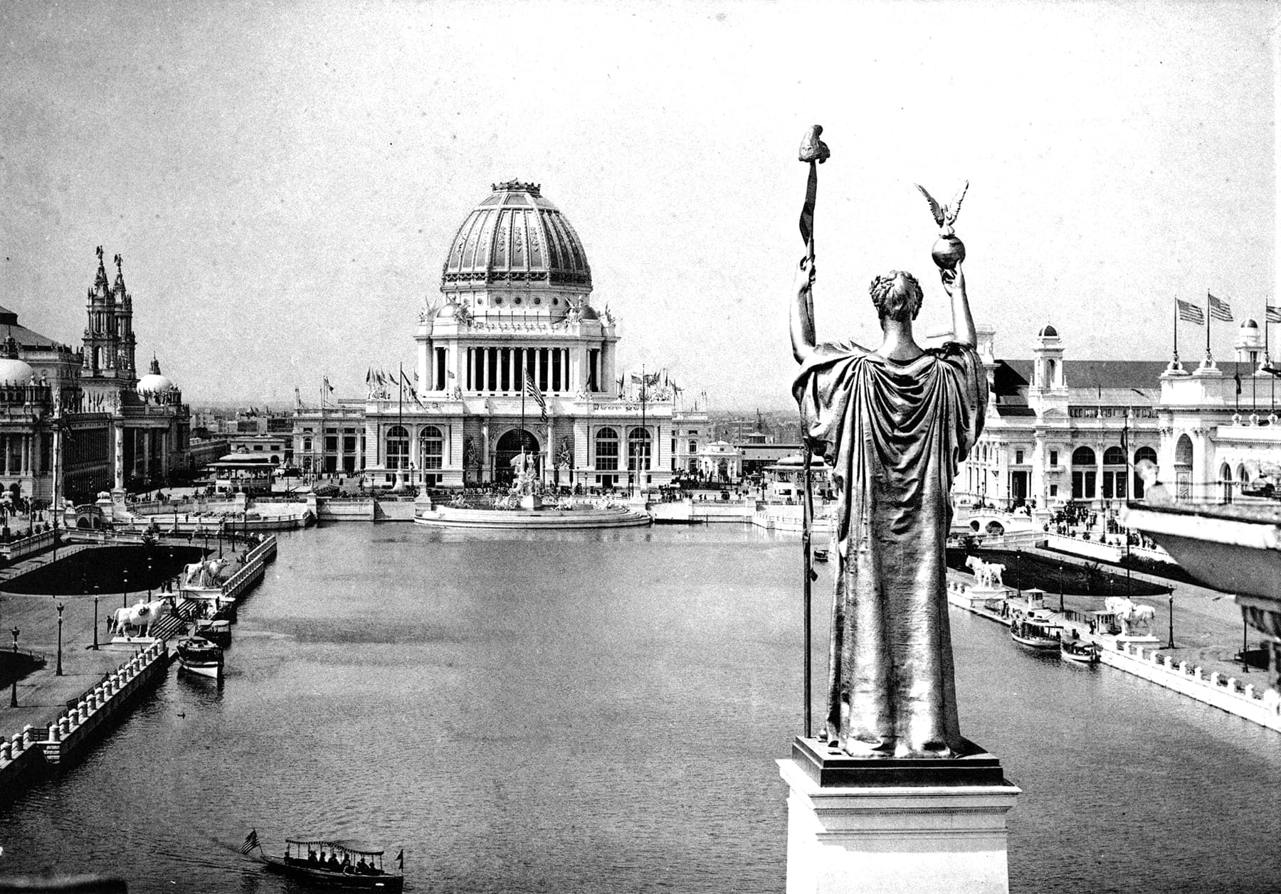 A black and white photo of a statue in front of a city