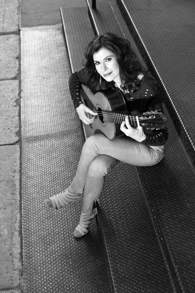 A woman sitting on a bench playing a guitar