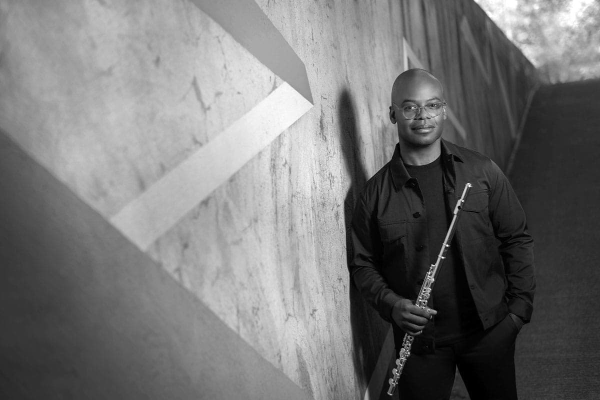 A man standing next to a wall holding a flute